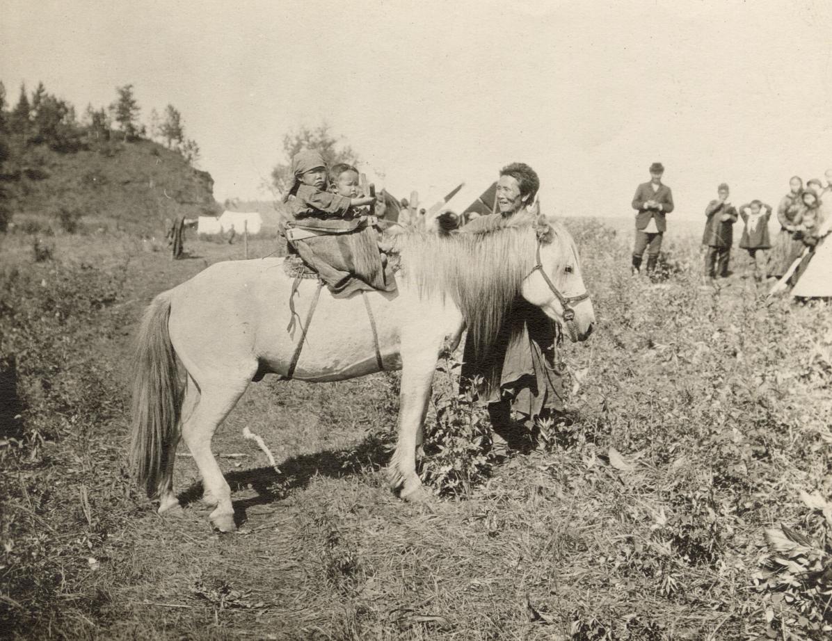 photo of two small children riding a horse with others looking on