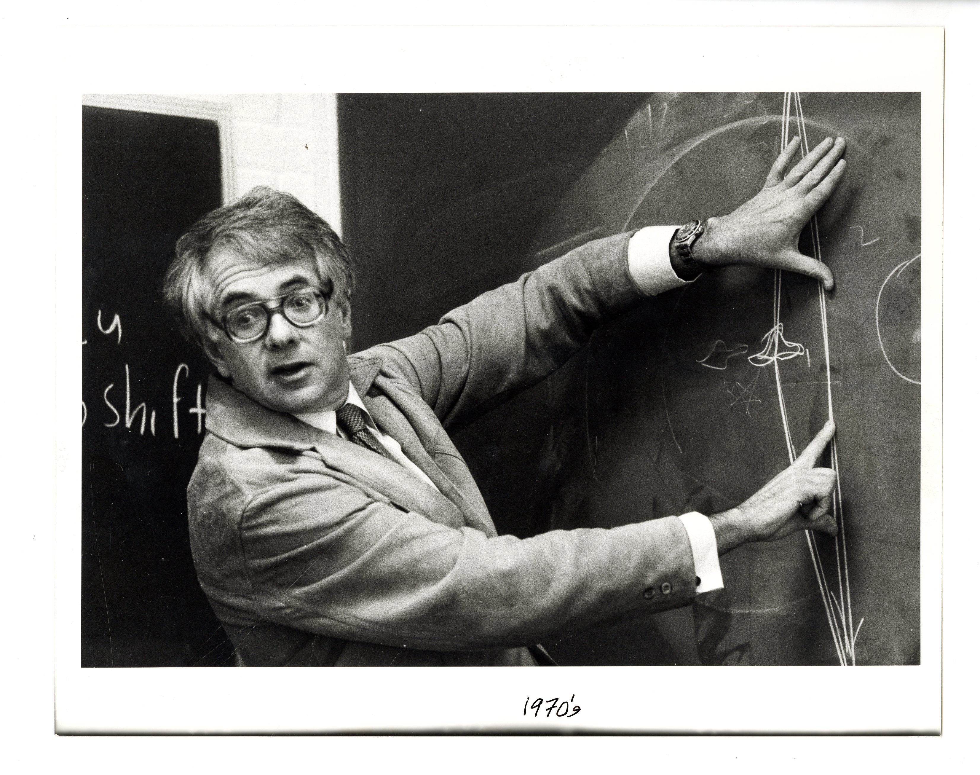 black and white photo of man pointing at chalkboard