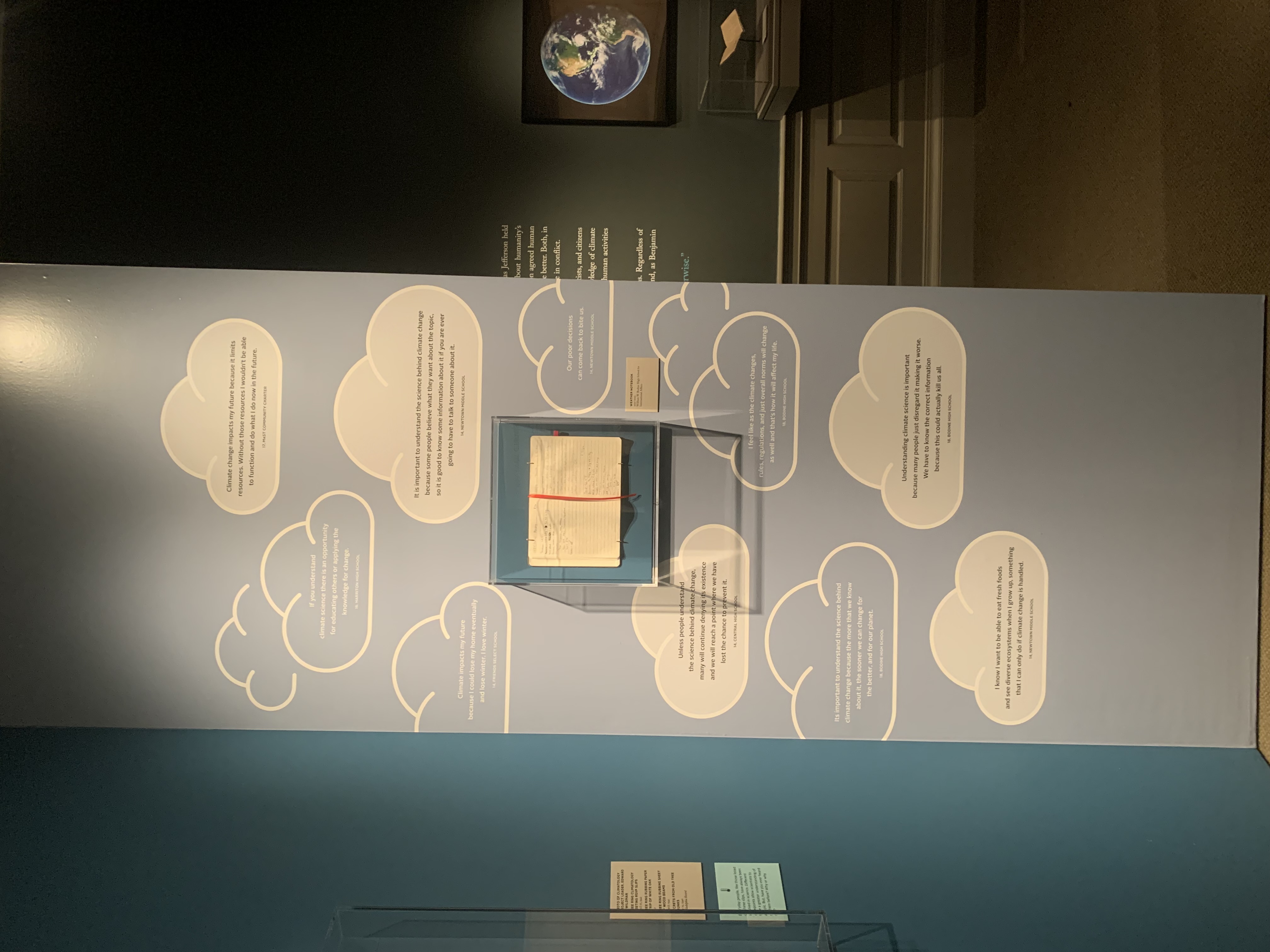 Photo of wall in exhibition that shows quotes and a journal from the Community Science Weather Data project