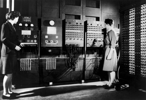 black and white photo of two women standing in front of ENIAC switches and cables