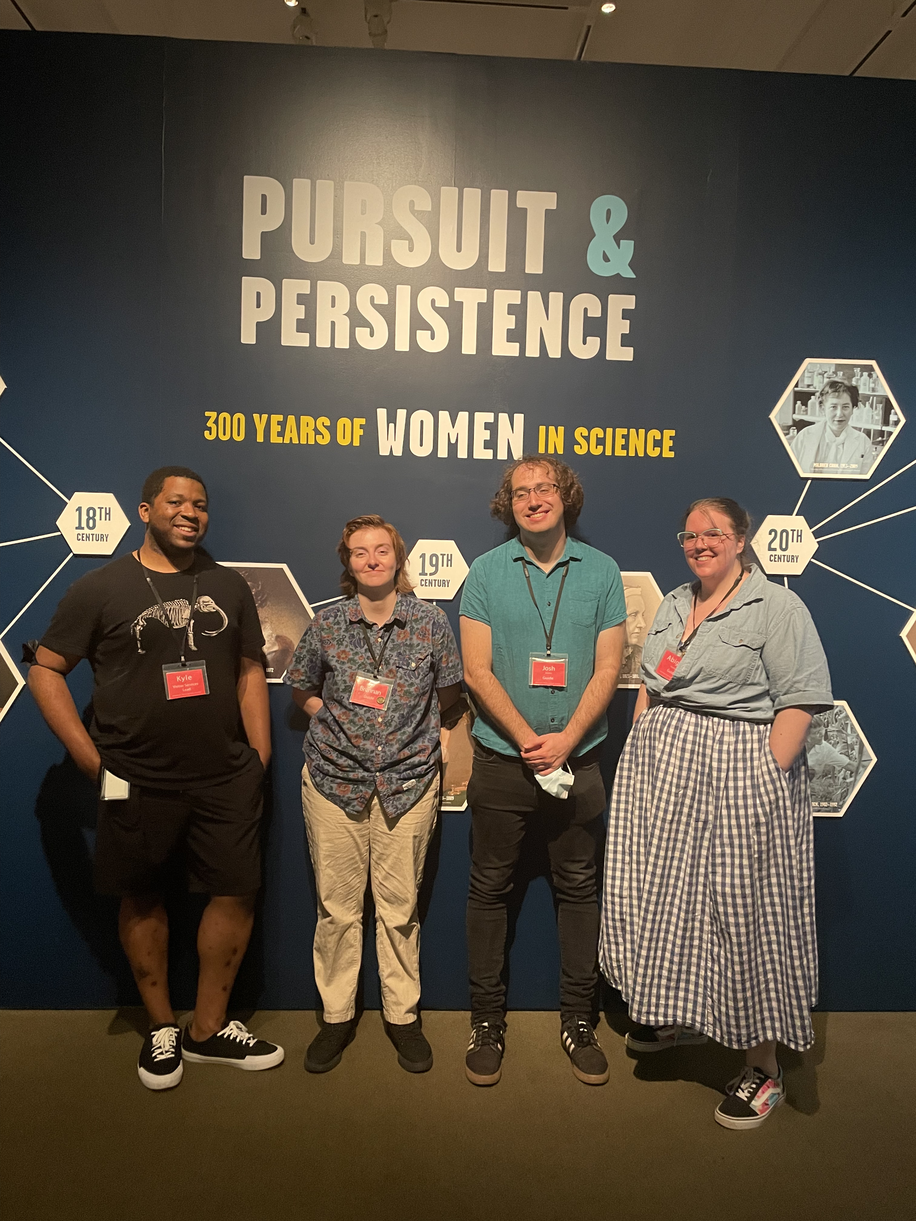 photo of 4 guides standing in museum gallery in front of Pursuit & Persistence title on wall