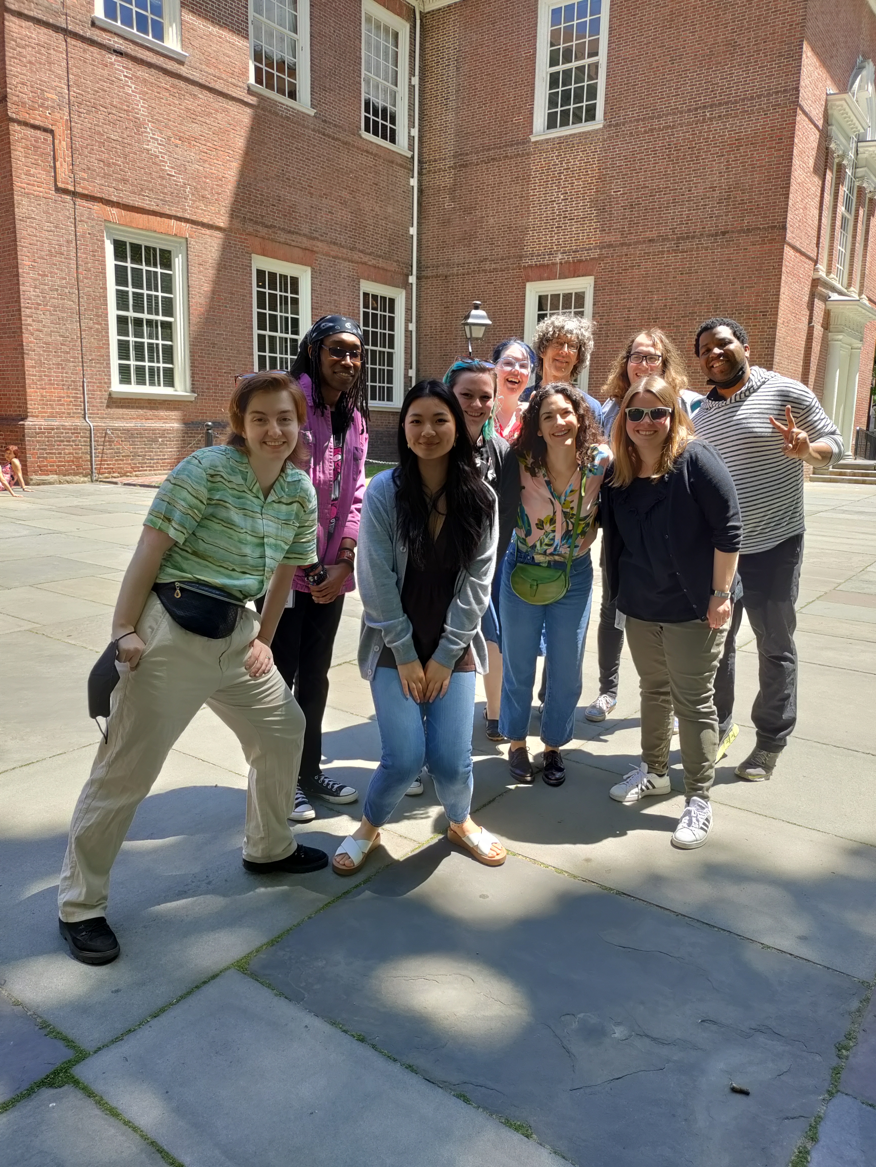 photo of 10 people standing outside in front of brick building on a sunny day