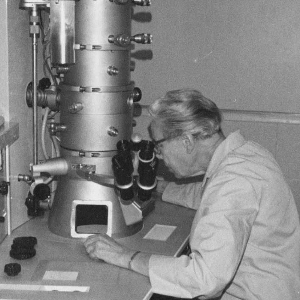 balck and white photo of woman seated at electron microscope