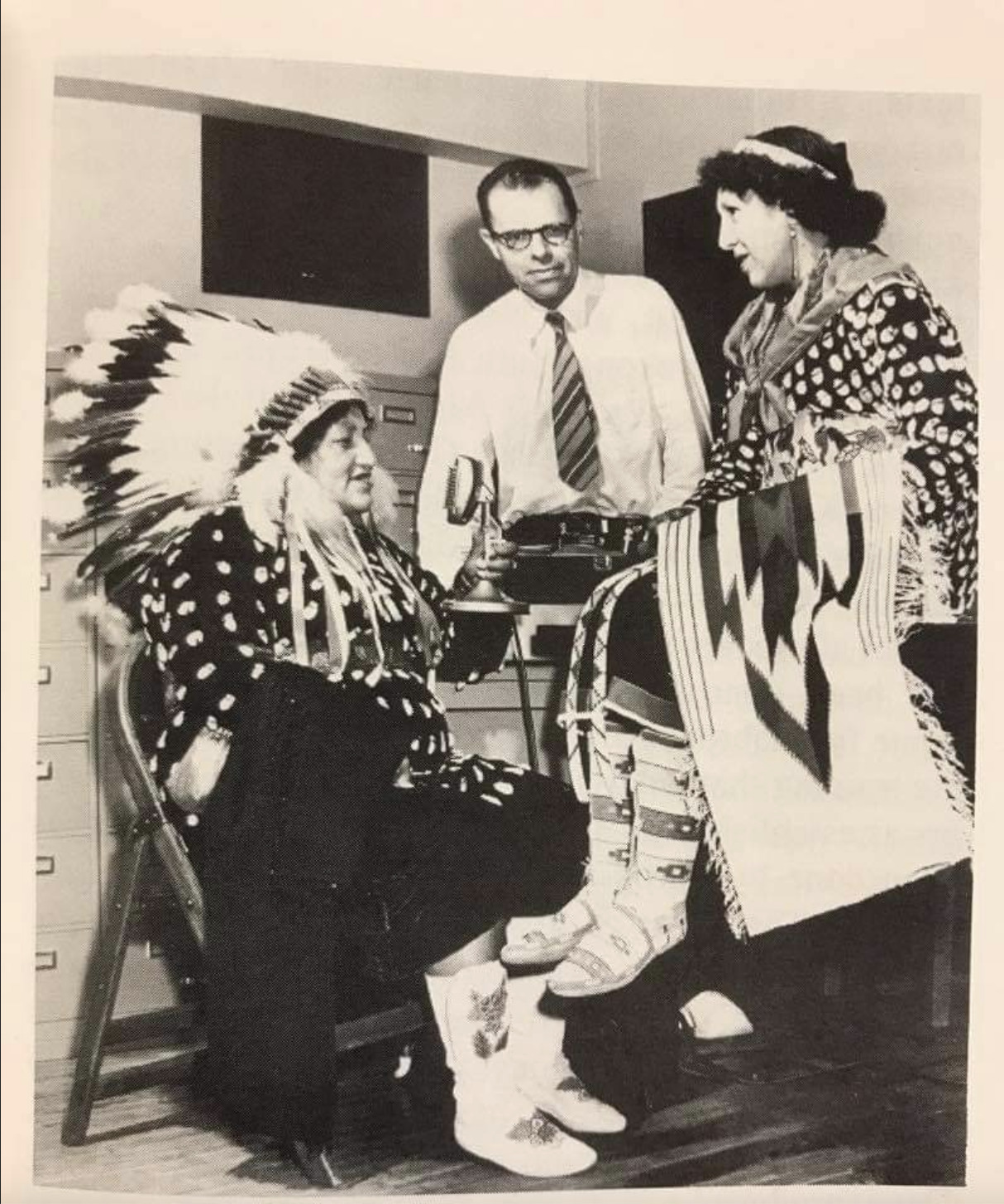 sepia toned photo of one woman seated left and two people standing talking to her