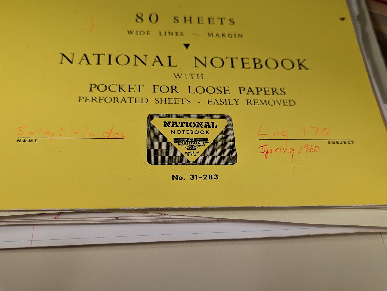 Photo of a bright yellow notebook cover, with sheets of paper poking out from underneath. Printed text on the notebook cover reads “80 sheets, wide lines - margin, national notebook with pocket for loose papers, perforated sheets - easily removed, [logo with ‘national notebook made in U.S.A], No. 31-283, name_____, _____subject”. In red ink ‘Sally McLendon’ is written on the line for “name” and ‘Ling 170, Spring 1960’ is written on the line for “subject”.