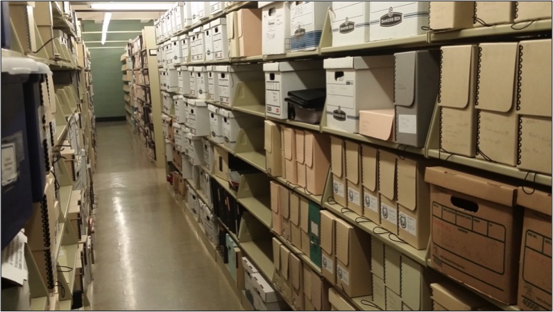 Una fotografía en color de filas de estanterías llenas de cajas de archivo de varios tamaños.