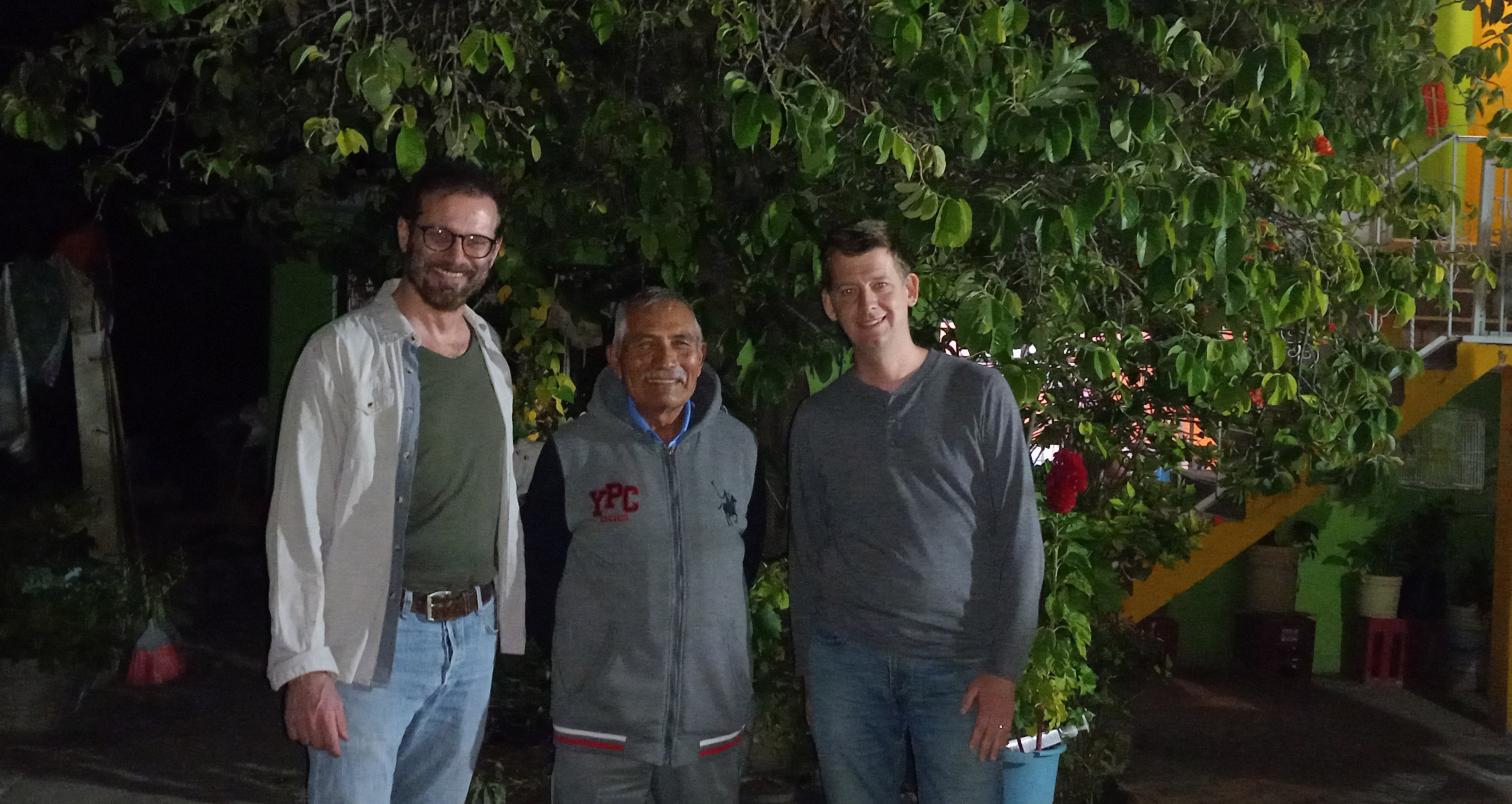 Tres hombres sonríen al fotografiarse frente a un árbol.