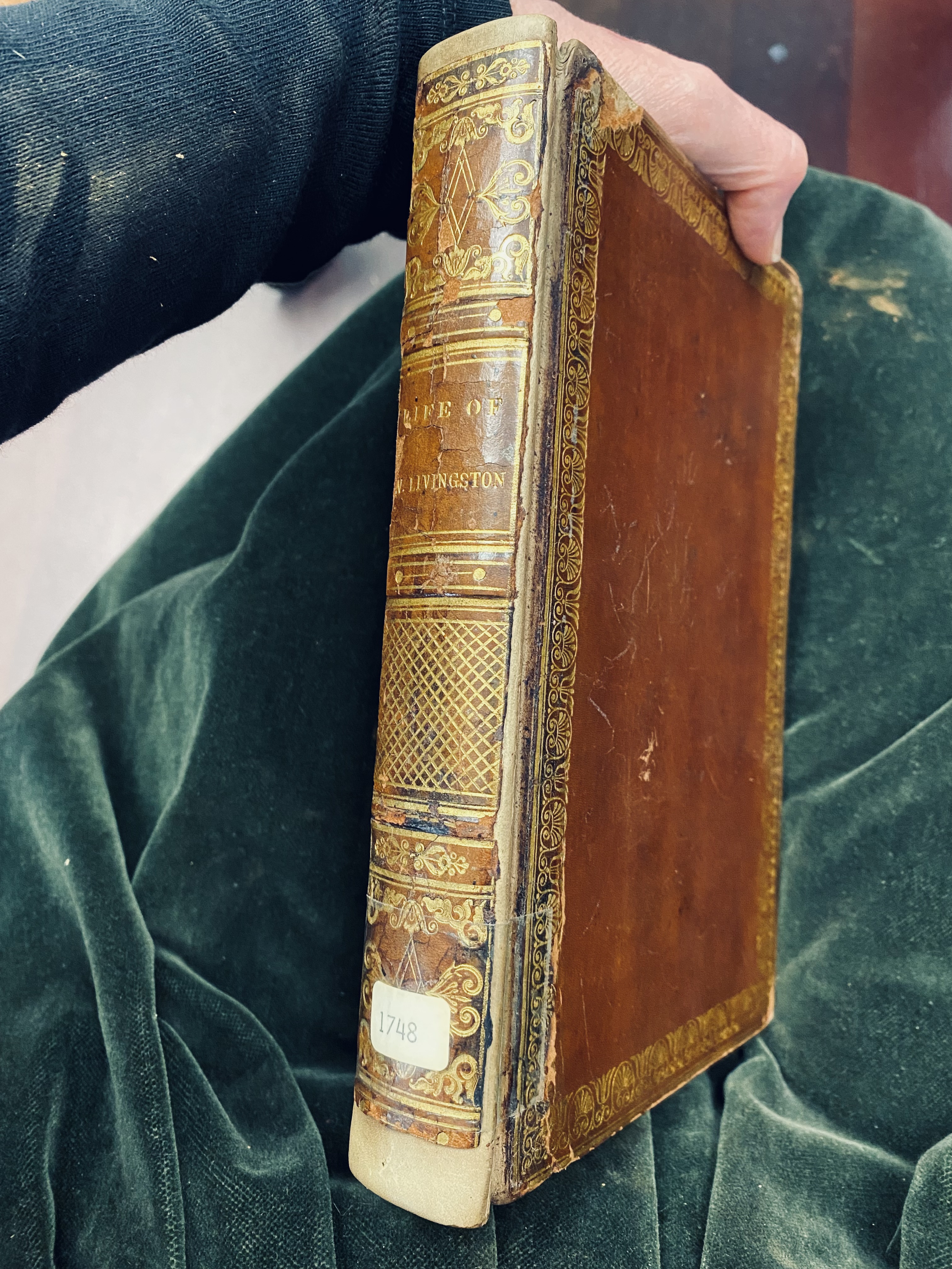 photo of book spine held by hand at top and velvet pillow beneath