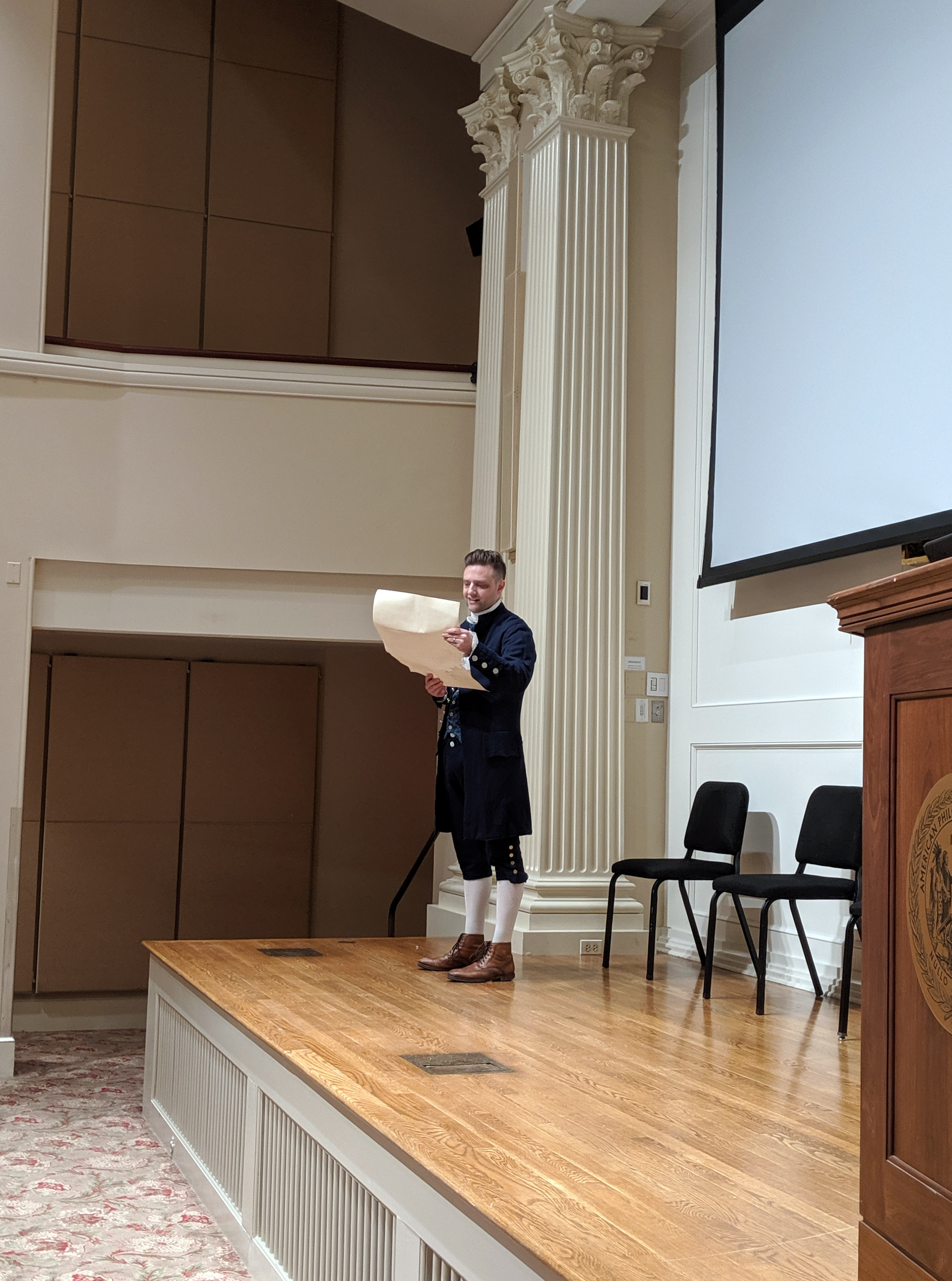 man in colonial outfit reading from large paper