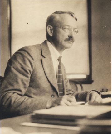 sepia toned photo of man seated at desk