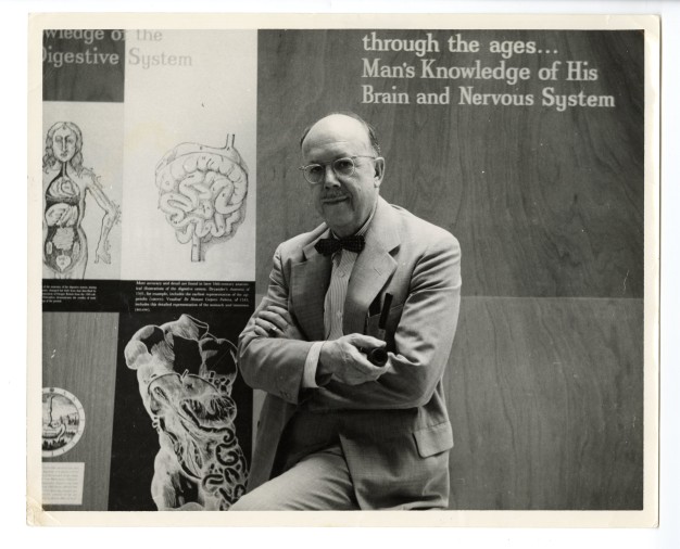 black-and-white photo of man in front of anatomy illustrations