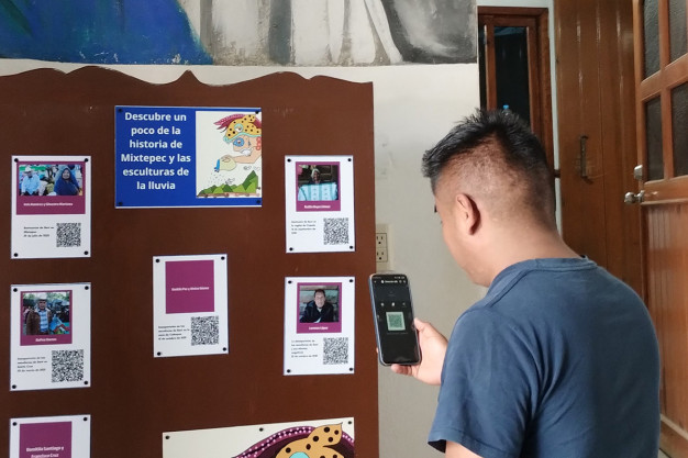 Un hombre con un teléfono escanea un código QR en un panel lleno de carteles coloridos.
