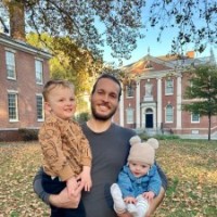 photo of man standing in park holding 2 children