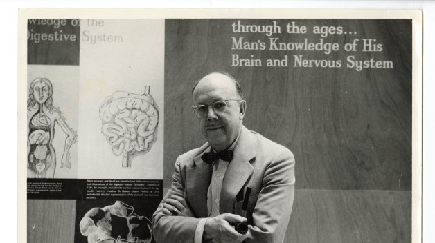 black-and-white photo of man in front of anatomy illustrations