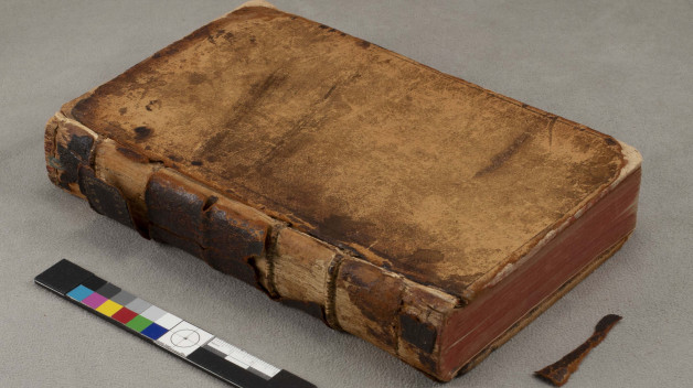 A worn leather-bound book on a gray table.