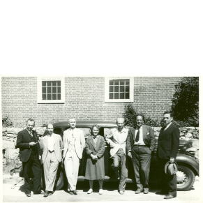 black and white photograph of group of seven people in front of a car parked beside a building, three men to each side of one woman (Barbara McClintock)