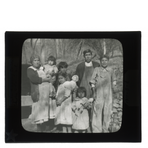 Black-and-white glass lantern slide of John and Nanny Driver and family standing outside.
