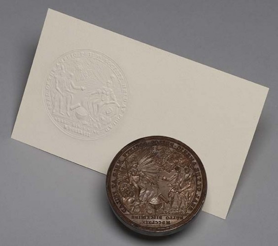circular engraved metal seal and white card with seal impression