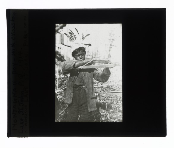 Black-and-white glass lantern slide of an Innu boy holding a crossbow at Lake St. John, Quebec.